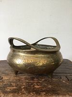 Front view of oval brass incense burner with detailed dragon engraving and raised handle on rustic wooden surface.