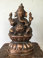 Front view showing detailed front features of seated copper statue including facial features, hands holding symbolic objects, and ornate pedestal base.