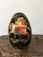 Front view of the vintage lacquered egg box showing painted figures of two women riding a brown horse against a black background with decorative accents.