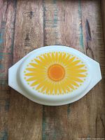 Top down view of white Pyrex lid with bright yellow and orange sunflower design
