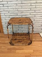 Front view of vintage rattan square side table showing two levels and rattan slat surface with some wear.