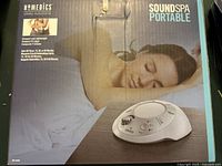 Photo showing front of the box with image of sound machine and a sleeping woman, highlighting compact and lightweight design.