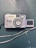 Front view of the Pentax Optio 330Gs digital camera showing lens, flash, and swivel LCD screen beside it.