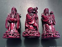 Front view of three red monk statues showing detailed robes and different poses.