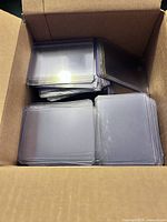 Box containing multiple stacks of clear, plastic trading card top loaders.