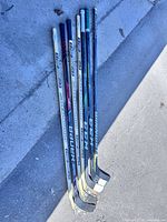 Seven right-handed hockey sticks laid on concrete, showing overall length and full sticks.