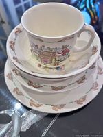 Stacked cup, two bowls, saucer and plate showing Bunnykins bunny motif around edges and detailed Bunnykins scene on the cup.