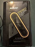 Front view of Sharp black stereo cassette player with gold and white design and volume dial visible.