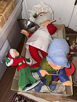 Four holiday-themed Annalee Dolls including Santa chef, Mrs. Claus, drummer boy, and reindeer in a cardboard box.
