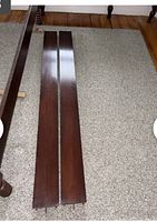 Photo of two long wooden side rails laid on the floor showcasing dark wood finish and minor wear.