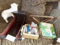 Lot items displayed on patterned fabric couch showing all items: doll cradle, sheep figure, toy ironing board, and boxed poodle toy with remote.