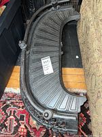 Full side and top view of curved antique cast iron fireplace fender with radial ridges and decorative edges.