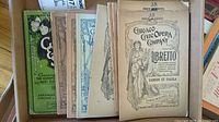 Seven antique opera librettos stacked, includes Chicago Civic Opera Company versions, one with green cover and others beige with ornate front illustrations.