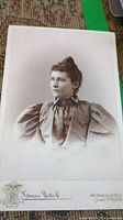 Close up of an antique portrait photograph of a woman in a puffed sleeve dress, sepia tone, mounted on card with 'Ashman Photo Co. Boston' imprint