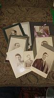 Array of antique portrait photographs on patterned fabric surface, showing portraits of men and women in vintage mounts and cards.