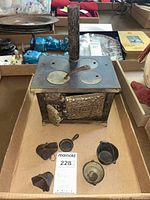 Front view of cast iron salesman sample stove with chimney and three stove top covers, includes small pans and shuttles in front.