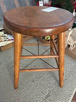 Antique round wood stool with four tapered legs and stretcher bars shown on a woven rug.