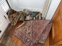 Three vintage rugs rolled and folded near a door with visible wear and moth damage
