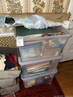 Stacked plastic storage bins containing various arts and crafts supplies including envelopes, markers, crayons, comics, and cutting mats.