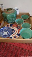 Group photo of all pieces including green vase, green bowls, large multicolored plate, and small blue and white bowl on cardboard.