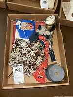 Box containing Asian puppet with painted face and fabric clothing, metal stand base, paper kimono and paper facial make-up cut-outs.