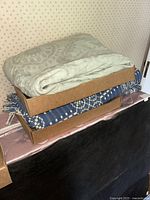 Two cardboard boxes stacked with folded blankets visible, showcasing multiple colors and patterns.
