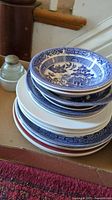 Stack of Blue Willow patterned blue and white bowls and plates, some plain white plates underneath