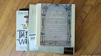Four books, including 'After the Revolution' with a decorated gray cover, shown inside a cardboard box on a wooden floor.