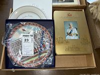 Overview of Royal Worcester Buckingham Palace plate, Queen's Golden Jubilee plate in packaging, and golden commemorative tin with Queen's portrait.