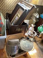 Two metal buckets with rust and patina, one with lid and handle, visible in front of wooden magazine rack filled with framed prints and photos