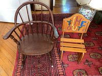 Children's dark wood Windsor style rocking chair with broken rocker and armrests next to light wood 'Time Out' chair on red patterned carpet.