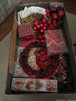 Full view of box with red berry wreath, assorted red berries and fruits, gold bead garland, red ribbons, and straw ornaments in packaging.