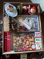 A box with Santa figurines, white Santa candle holder, wooden nativity set, wrapped candles, and I Spy Christmas puzzle visible.