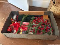 Box containing Santa outfit, artificial red berries, nutcracker ornament, Christmas paper goods