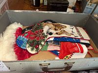Photo showing several Christmas stockings stacked in a metal container with a red and white Santa hat on side. Stockings have diverse colorful holiday designs including a corgi dog and holiday bows.