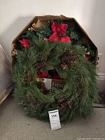 Photo showing the Fresco Poinsettia wreath featuring red poinsettia flowers and green pine foliage inside a box.