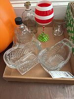 Clear glass Santa bottle with embossed details, red and white striped Christmas goblet, two sled-shaped glass bowls, and two other glass bottles arranged in a cardboard box.