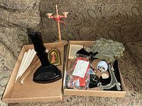 Photo showing a collection of items including wooden candle holder, Braun clock, glasses, roller light, plate holders, and a heart-shaped decoration on a patterned fabric background.