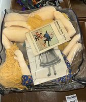 Doll making kit components inside clear plastic bag including fabric doll parts and a booklet titled 'Making Soft Toys'.