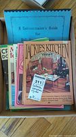 Photo of the collection showing various instruction booklets including 'Jackie's Kitchen Volume 1' and 'A Cabinetmaker's Guide for Dollhouse Furniture' with several other colorful booklets stacked underneath.