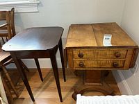 Photo showing a dark wood small drop leaf side table and a light wood side table with drawers placed side by side.