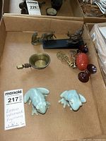 Box containing two light blue ceramic frog figurines and various brass and wooden decorative items, including a brass melting pot and figurines.