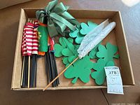 Photo of box containing small flags on black sticks as well as loose green shamrock shapes and one white patterned stick.