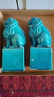 Side view of the pair of turquoise ceramic Foo Dogs showing detailed carving and square pedestal bases.
