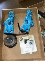Two blue ceramic Foo Dogs bookends with carved bases, viewed from the side in a cardboard box along with other items.