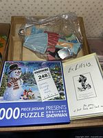 Photo showing the snowman puzzle box, paper dolls in plastic bag, and Ex Libris game in beige box.