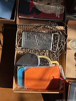 Lot of wire cooling racks, several kitchen graters, small colored cutting boards arranged in a box under sunlight