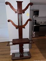 Full view of wooden hall tree with center mirror, curved wooden hooks, shelf below hooks, and tray base below shelf.