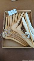 Box with six natural wood hangers and two padded white fabric hangers with hooks.