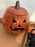 Front view of ceramic Jack O Lantern pumpkin with face cutouts seated on a surface.